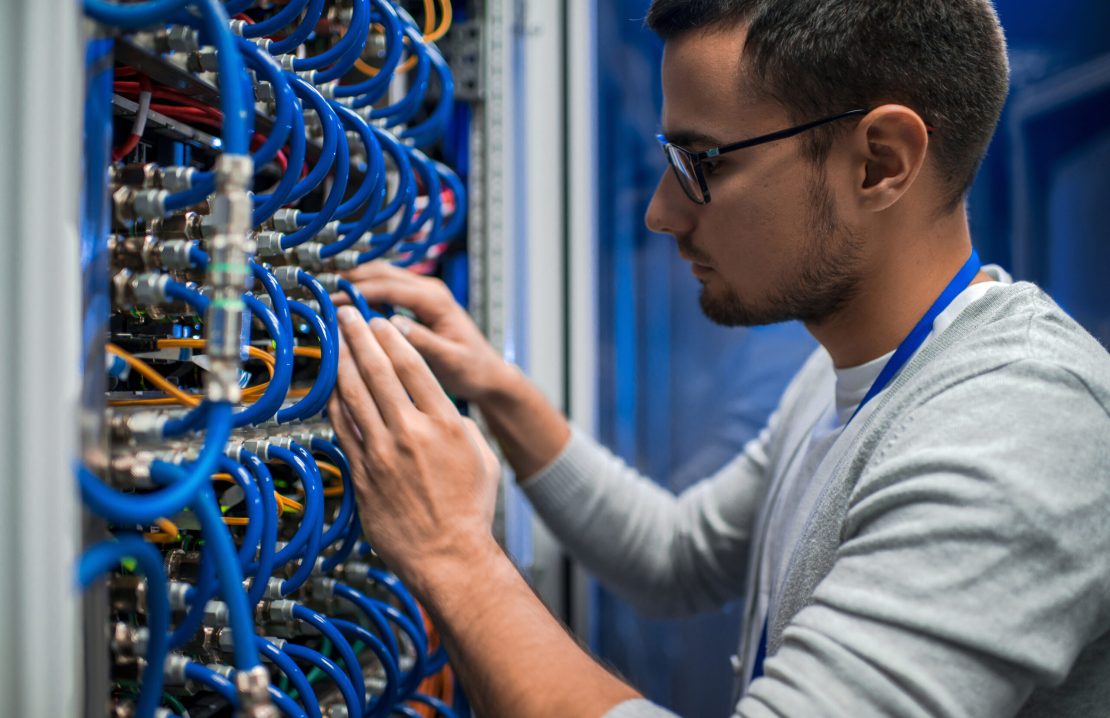 Side view portrait of young man connecting wires in server cabinet while working with supercomputer in data center